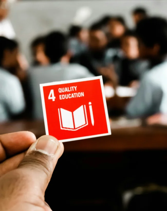 SDG 4 (Quality Education) cutout being held up with a classroom in the background